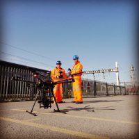 Two RUAS trained drone pilots holding drone radio transmitters with a drone set up in front of them to capture some aerial imagery.