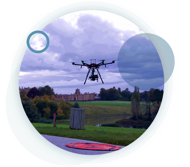 A circular gif containing an airborne drone at a national trust park during an aerial inspection.