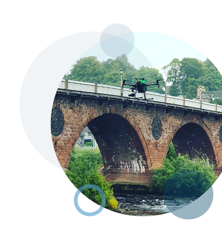 A circular image containing an airborne drone flying above a river and small bridge, during an aerial inspection.