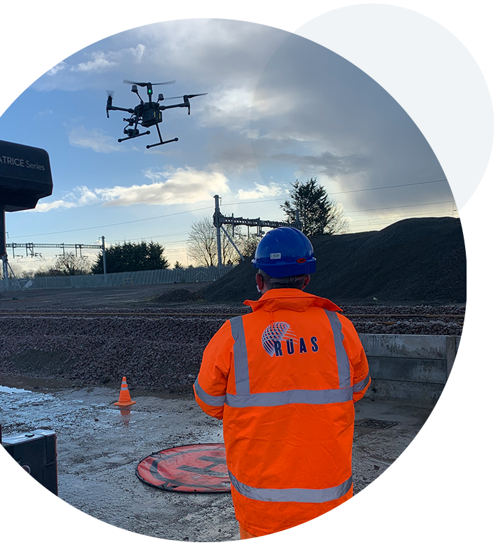 A circular image of a RUAS trained pilot, flying a drone during a construction survey.