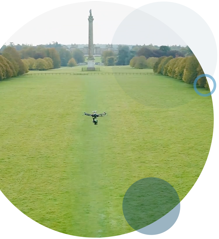 A circular gif of an airborne drone at a national trust park, performing an aerial inspection, with a manor house in the landscape.