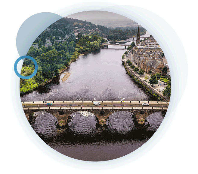 A circular gif containing drone imagery of a bridge running over a large river, with cities either side.