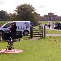 The RUAS team preparing a drone for takeoff at a national trust park with a beautiful, large, manor house in the back.