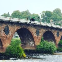 An airborne drone being flown over a river with a bridge in the background during an A2 CofC and GVC RUAS training course.