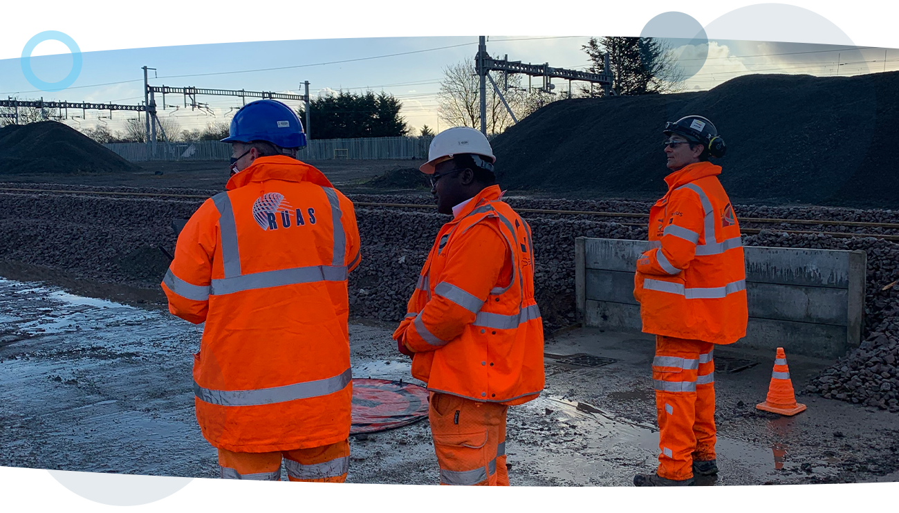 Three RUAS trained drone pilots in high vis suits, stood at a power plant.