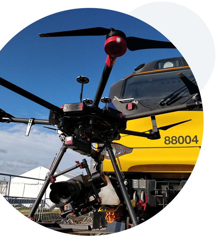 A circular close up shot of a drone, with a train in the back, preparing for take-off during the survey of a railway station