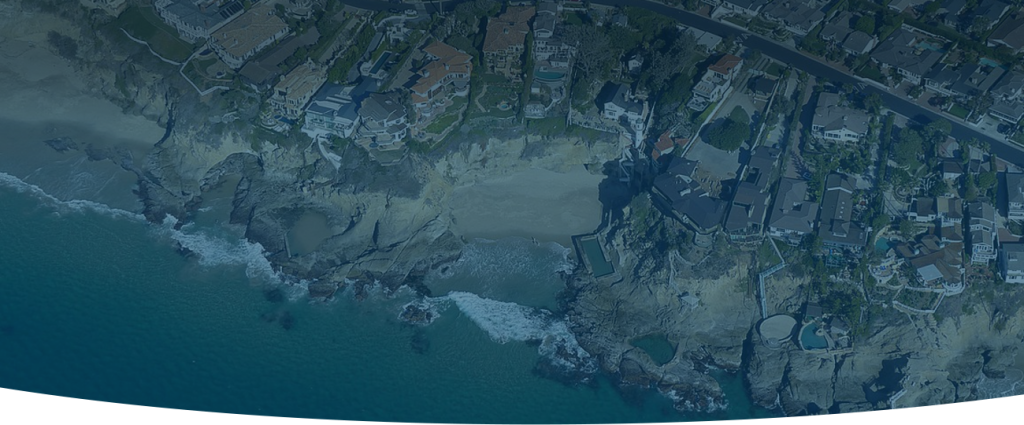 A dimmed, aerial shot of a coast-line with houses on the edge, as well as a private beach, during a thermal inspection.