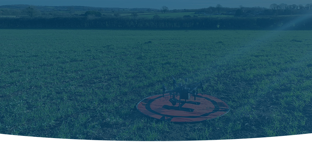 A darkened image of a drone in a field, preparing to take off and produce a topographical survey.