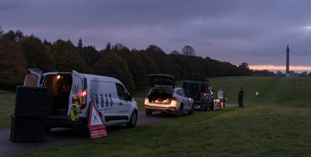 Three vans at a national trust park, during the early morning. A drone is being prepared to perform a topographical survey.