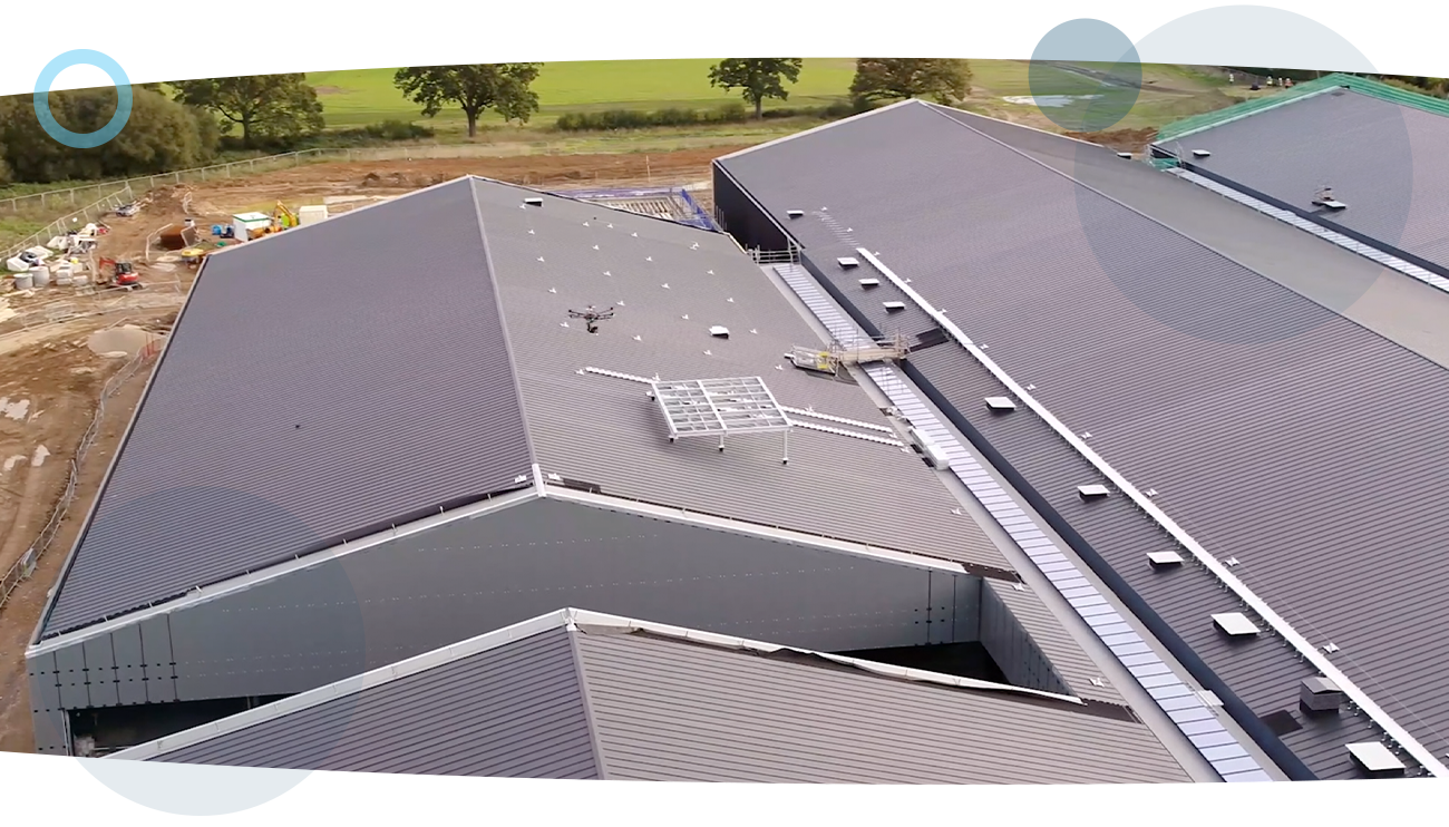 An aerial shot of a drone inspecting the roofing of a warehouse, during an oil and gas inspection on a construction site, run by a RUAS trained drone pilot.