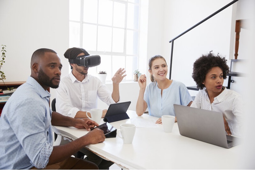 Four people sat round a business office table, with one in 360 VR, and the others watching.