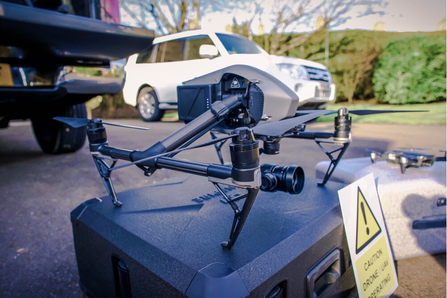 A black drone sat on a drone case with a warning sign leant on it, implies operating drones can be expensive.