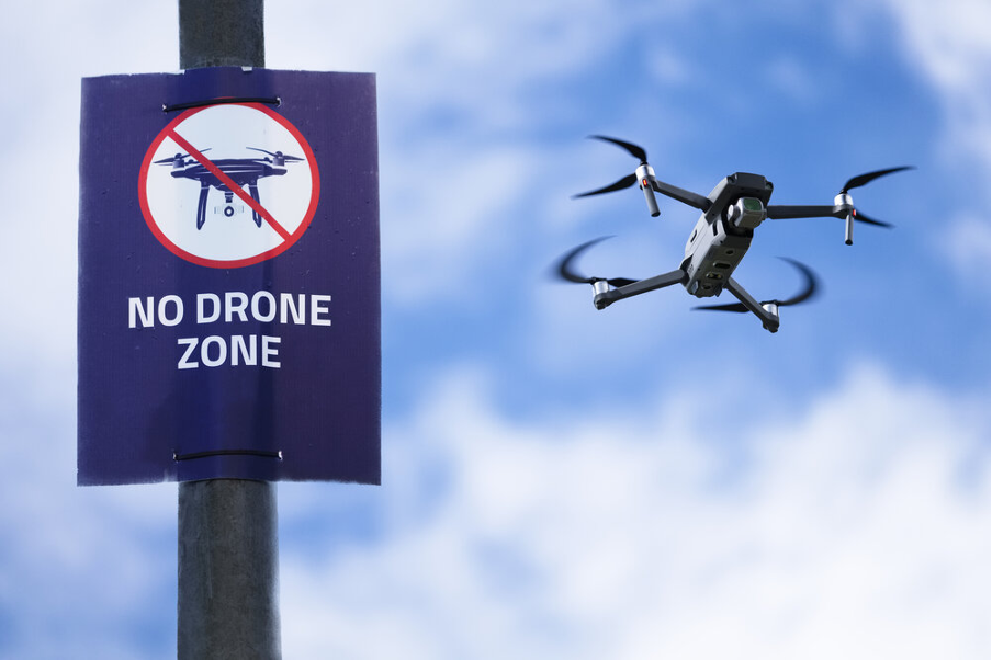 An airborne drone next to a no drone zone sign raises the question as to whether the drone is registered.