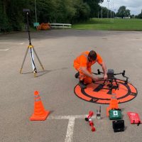 A man wearing a high vis RUAS suit preparing a drone for EVLOS training.