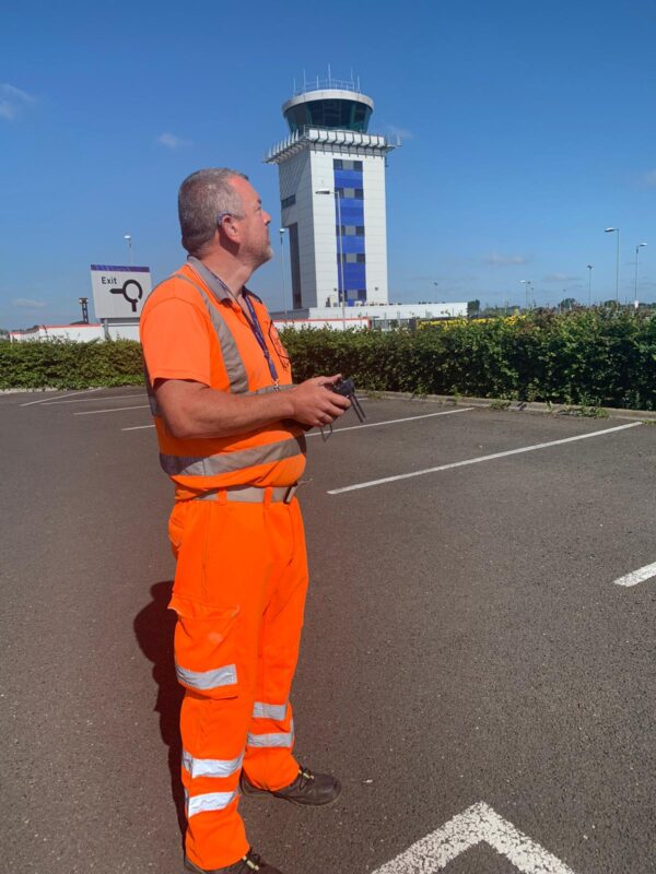 A man wearing a high vis suit controlling a drone using a drone radio controller at Southend Airport's RPZ.