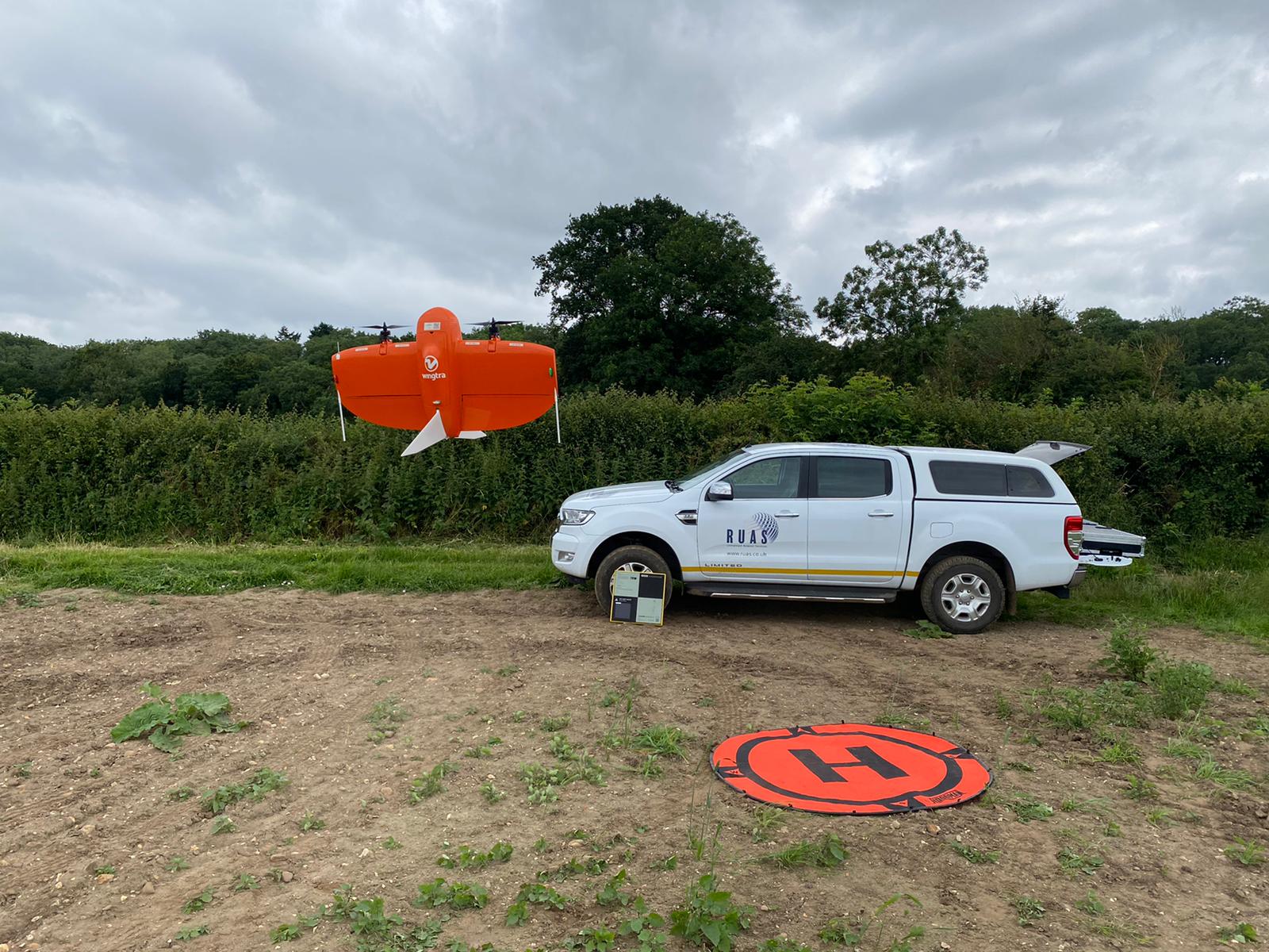 A drone taking off in the middle of a field with a RUAS truck in the back. This depicts the difference of VLOS, EVLOS and BVLOS.