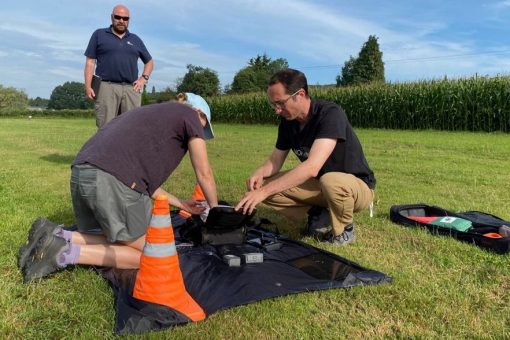 There are three men setting up a drone in the middle of a field. This is the GVC training course.