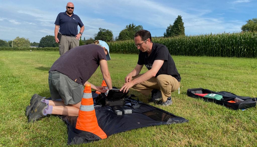 There are three men setting up a drone in the middle of a field. This is the GVC training course.