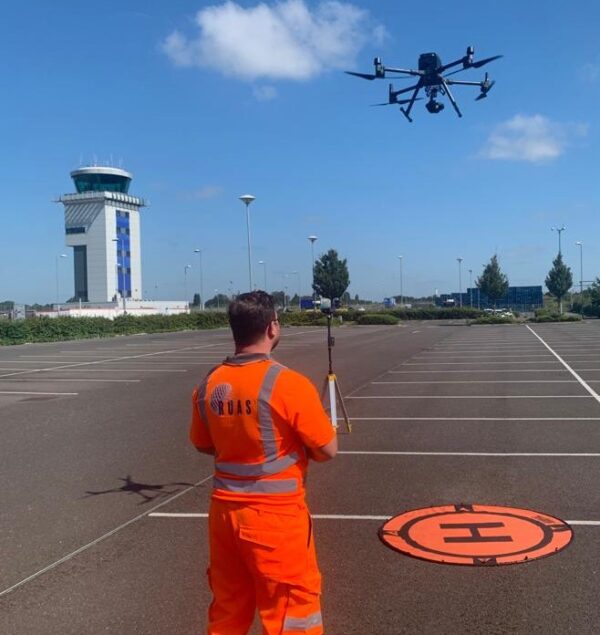A man wearing an orange high vis RUAS suit at an airport, flying a drone. This shows the importance of flight restriction zones.